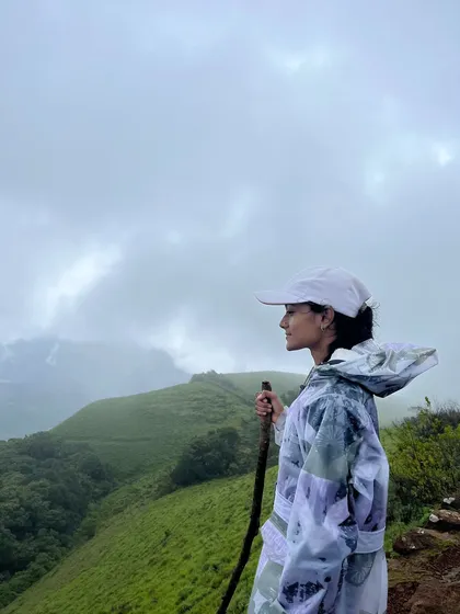 A trekker in a stylish raincoat looks out over the misty green hills of Bandaje.