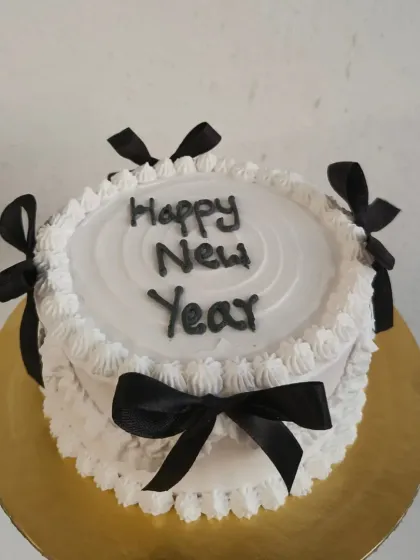 An elegant black and white themed cake for a stylish New Year's Eve party. The cake is decorated with delicate piping and black satin ribbons.