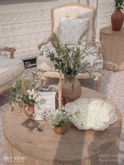 A coffee table styled with bowls of white flower petals, rustic vases, and framed art, all in a cohesive and serene color palette.