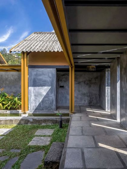 A covered walkway with a stone floor and raw concrete walls offers a play of light and shadow. This passage connects different parts of the cafe while providing a sheltered transition space that opens to the garden.