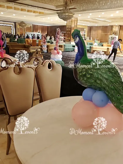 A peacock-themed table centerpiece. A large peacock foil balloon sits on a base of pink and blue balloons, perfectly complementing the Krishna theme of the party.