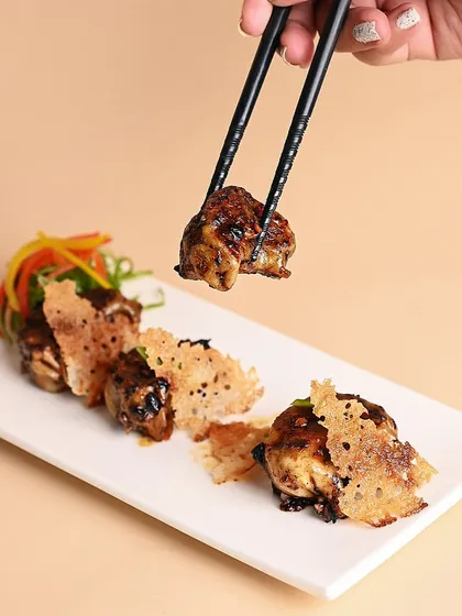 A single, beautifully glazed gyoza held by chopsticks. This shot highlights the glossy sauce and the delicate parmesan crisp that accompanies our pan-fried dumplings.