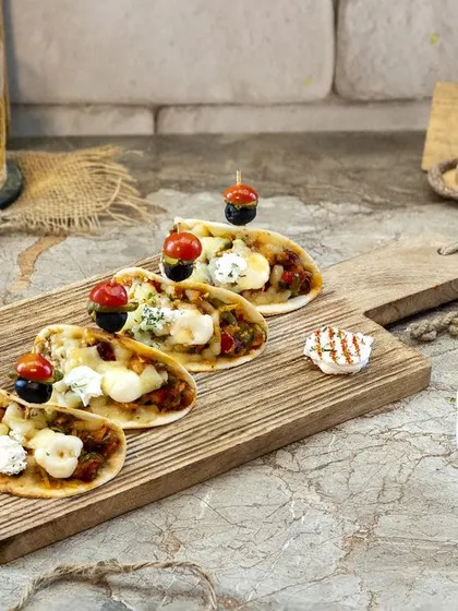 These mini naan pizzas were shot to look like the perfect shareable appetizer. The composition on the wooden board with fresh ingredients scattered around gives a relaxed, social vibe, ideal for a cafe or bar menu.