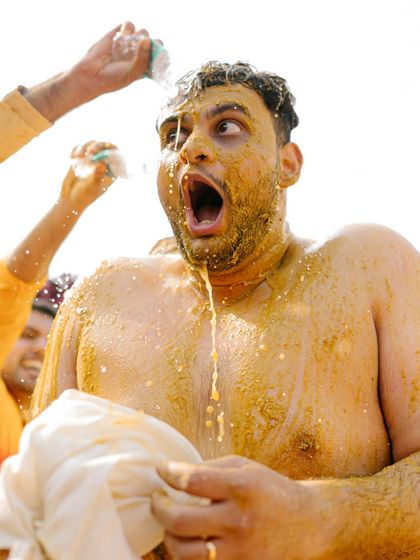 A raw, candid shot of the groom's shocked and joyful expression as he gets drenched during the Haldi.