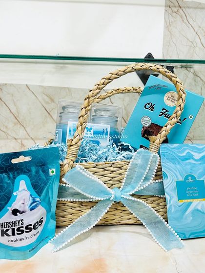 A beautiful pastel blue hamper for a new mom, filled with Hershey's Kisses, fudge, and soothing hand cream, all packed in a natural grass basket.