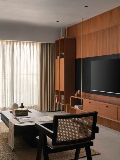The living room is designed for both relaxation and entertainment, with a custom teak wood veneer TV unit that features integrated shelving. The clean lines and natural materials keep the space feeling open and uncluttered.