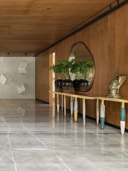 The vast entrance lobby of the K Residence, featuring a console with uniquely crafted monolithic marble legs. The space is designed to be an art gallery, with a contemporary brass mirror reflecting an installation on the opposite wall.