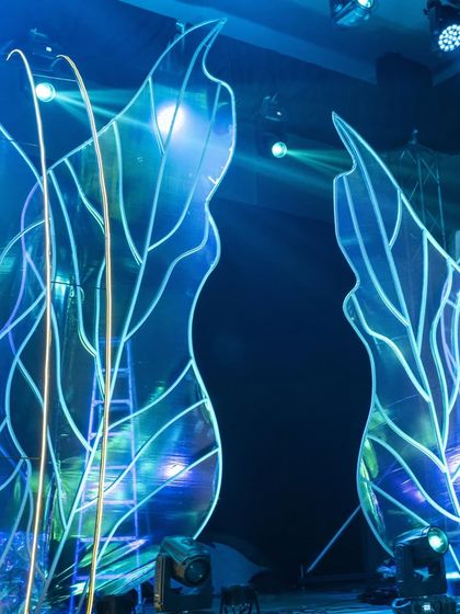 A close-up of the abstract, illuminated leaf structures on the stage. The internal lighting and iridescent material create a beautiful play of light and color.