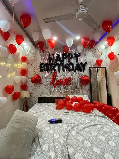 This is a wide view of a popular romantic birthday setup I offer. I cover the ceiling with red and white balloons, create a feature wall with a silver fringe curtain and bold 'Happy Birthday' lettering, and scatter more balloons on the bed to complete the immersive surprise experience.