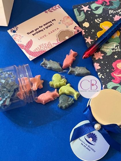 A closer look at the contents of our mermaid-themed return favours. We include a jar of our handmade, ocean-shaped chocolates, a themed diary and pen, and a personalised thank you card.