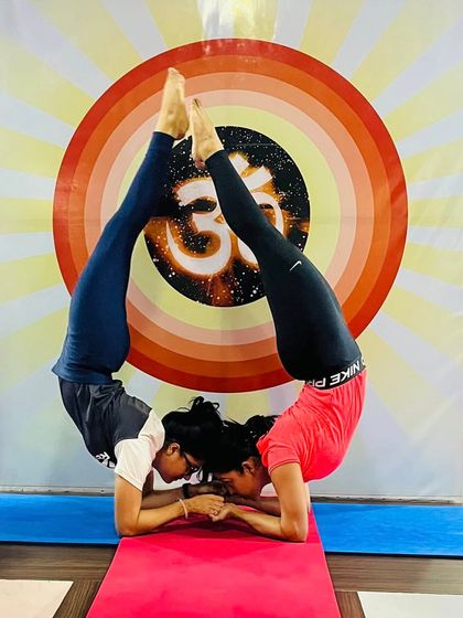 Two students create a perfect circle with their bodies in this synchronized partner Scorpion Pose. This advanced inversion highlights incredible flexibility and balance.