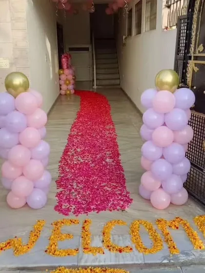 A beautiful and traditional welcome entrance for a baby. The path is decorated with a carpet of fresh flower petals, flanked by pink and lilac balloon pillars, and a 'WELCOME' message written with marigold flowers.