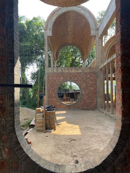 Looking through an oval aperture at the House of Verses during construction. This view highlights the project's narrative spirit, with its series of arches and vaults creating a dreamscape that connects to the surrounding paddy fields.