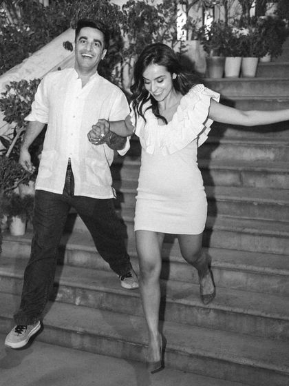 A playful black and white photo of a couple jumping down the stairs together, hand-in-hand.
