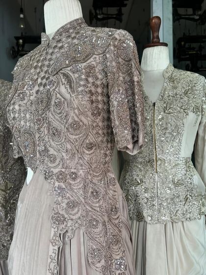 A close-up of a heavily embellished ensemble, featuring intricate beadwork and embroidery in a peacock-inspired pattern on a muted grey fabric.