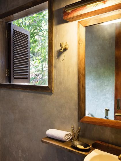 The bathroom of the Garden Room, with its cement-plastered walls and a window that opens to the lush greenery outside.