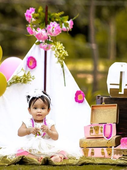 A lovely outdoor first birthday scene, with the little one sitting in front of a decorative teepee before the cake smash begins.
