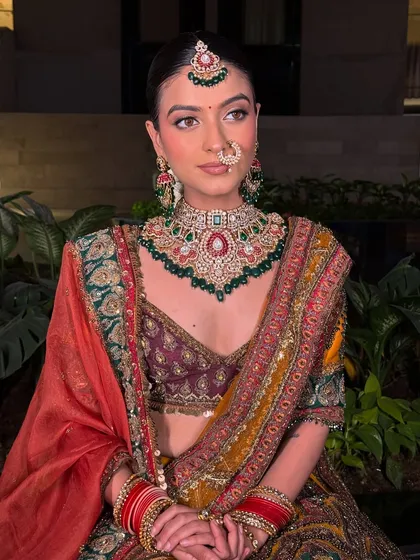 A full-length view of the bride seated, looking absolutely regal in her multi-colored lehenga and heavy polki jewellery set. The red bangles add a perfect traditional touch.