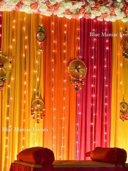A close-up of the Mehendi night decoration on a home terrace, showing the warm lighting and traditional hangings against the colorful drapes.