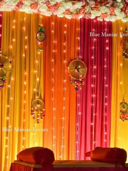 A close-up of the Mehendi night decoration on a home terrace, showing the warm lighting and traditional hangings against the colorful drapes.