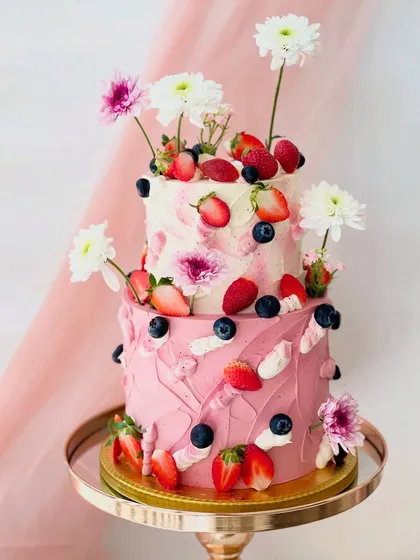 This vibrant two-tiered cake showcases a playful yet elegant design with textured pink buttercream, fresh strawberries, blueberries, and white chrysanthemums. It's a perfect example of how I combine fresh flavours and artistic decoration.