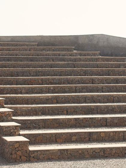 The tiered seating of the amphitheater, constructed with local stone and gravel. This public space is designed for community gatherings, performances, and environmental education, fully embracing its role within the biodiversity park.