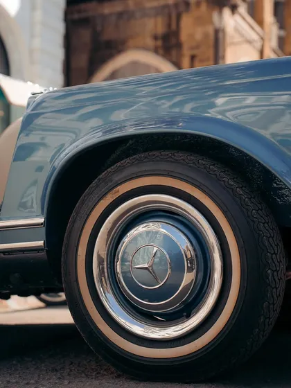 A detailed shot of the wheel of a vintage Mercedes-Benz. The chrome hubcap and whitewall tire are details that speak of classic luxury and design.