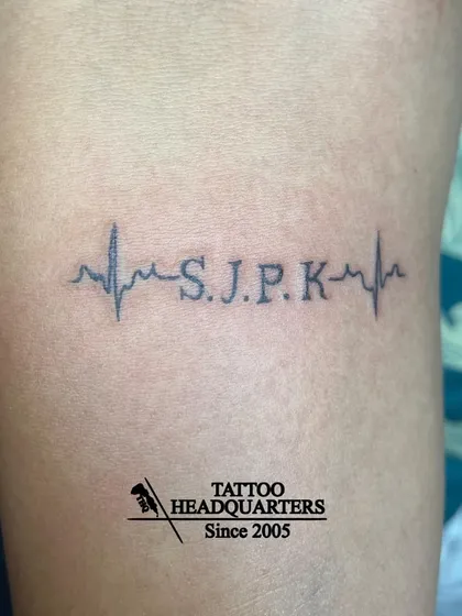 A heartbeat (EKG) line tattoo with the initials "S.J.P.K" integrated into the rhythm.