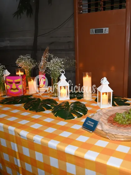 Rooted in nature, wrapped in detail. A tablescape from our tribal-themed celebration, featuring a checkered tablecloth, monstera leaves, and candle-lit lanterns.