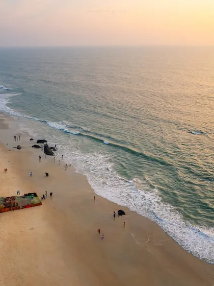 An aerial view of a shipwreck on the shores of Padubidri beach. The golden light of sunset illuminates the scene, creating a poignant image of this man-made structure reclaimed by the sea.