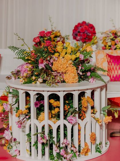A unique floral arrangement where flowers seem to burst from within a white, slatted side table. This creative design adds an element of surprise and artistry to the decor.
