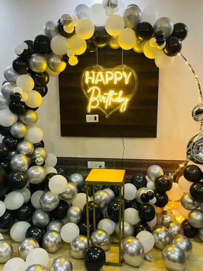 A sleek black and silver balloon arch for a 22nd birthday. The setup includes a heart-shaped neon sign and foil numbers for the age.