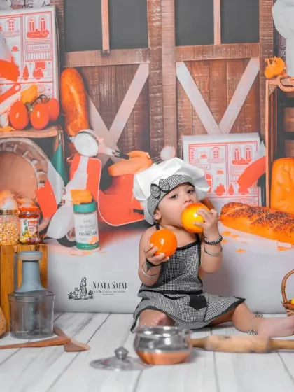 The entire kitchen set is designed to be a playground. Here, the baby is surrounded by a colorful assortment of props, from a toy scooter to loaves of bread, creating a vibrant backdrop.