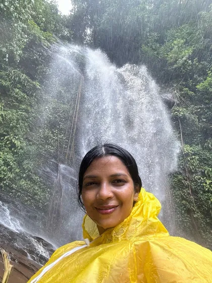 A happy trekker in a raincoat poses in front of a beautiful waterfall. Our monsoon treks are all about embracing nature in its rawest form.