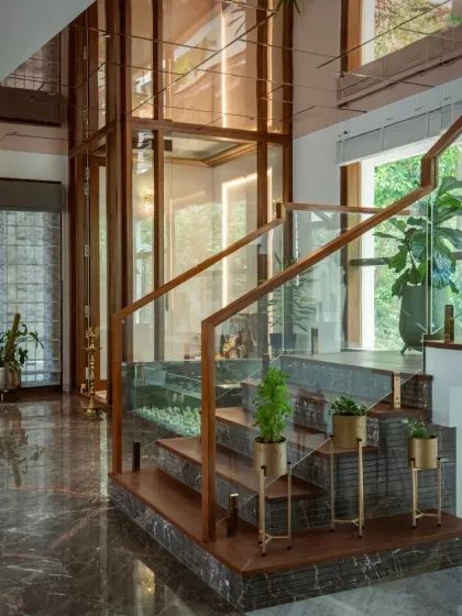 Views of the staircase adjacent to the pooja room, showing the combination of dark marble, wood treads, and glass railings that create a warm yet modern aesthetic.
