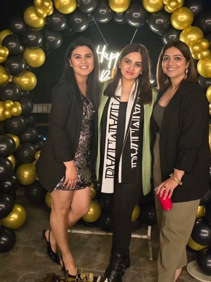 Friends gathering for a photo in front of the black and gold balloon arch at a terrace party.