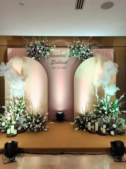 Soft, romantic, and elegant, this stage design uses blush-pink arched panels and delicate floral arrangements. The addition of whimsical white tulle bows and warm uplighting creates a fairytale setting for an engagement or reception.