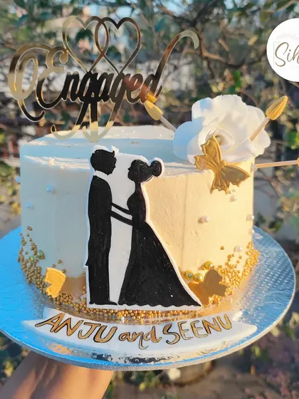 Promises of love. This elegant engagement cake features a hand-drawn couple silhouette, gold accents, and a beautiful "Engaged" topper, creating a sophisticated and personal design.