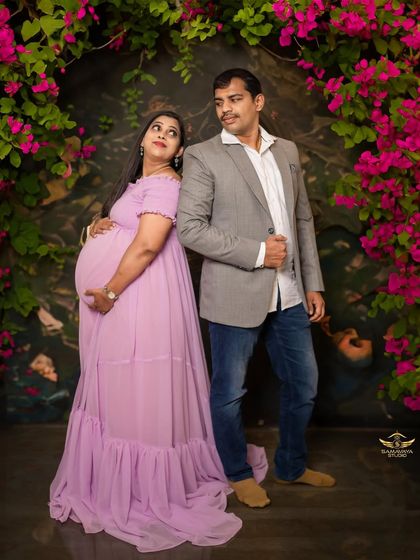 A fun and playful pose from a couple during their studio maternity session. Her lavender gown pops against the floral archway.