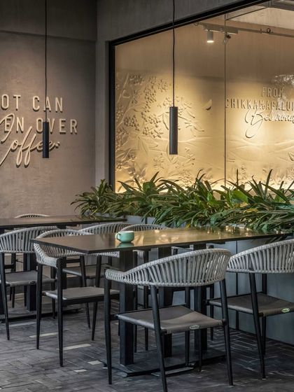 The outdoor area features modern, woven chairs that are both durable and stylish. The iconic tagline on the wall is visible from the outside, inviting passersby to step in.