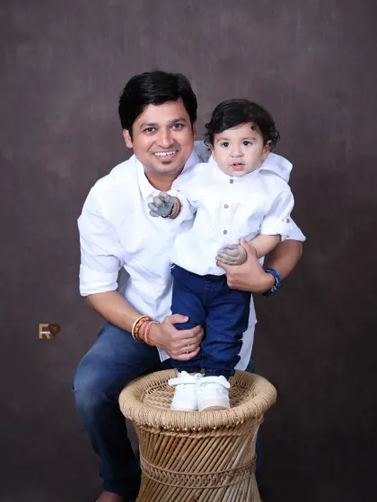 A proud father holds his son, who is standing on a wicker stool. This portrait captures a lovely moment between father and son, showcasing their bond as the child grows.