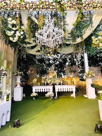 A stunning decor piece featuring a large chandelier under a canopy of lush greenery and white flowers.