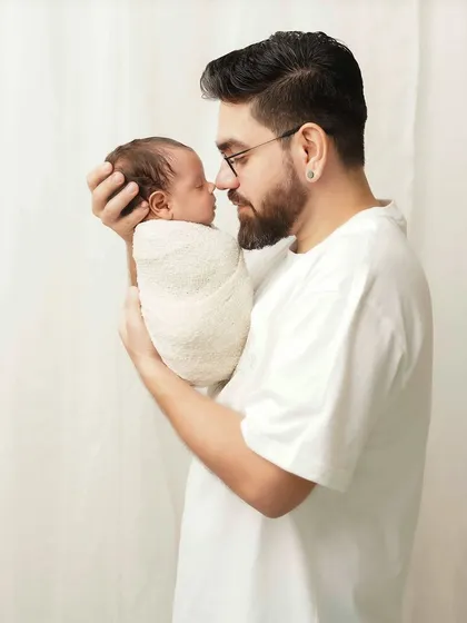 A father holds his newborn, sharing a quiet, nose-to-nose moment. The high-key lighting and white outfits give this portrait a soft and dreamy feel.