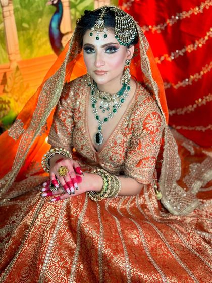 The full view of the orange and green Pakistani bridal outfit. The makeup complements the colors of the dress perfectly.