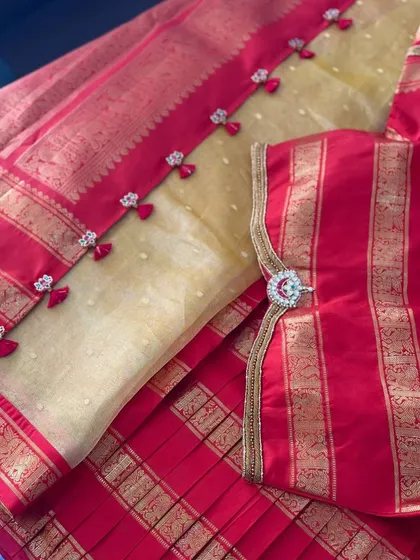 A close-up of the blouse sleeve, featuring a circular Jadau pendant set on a traditional gold border.