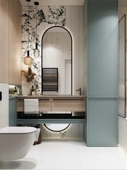 In this bathroom, I combined multiple textures to create a rich, tactile experience. The design features light wood, book-matched marble, and pastel green fluted panels for storage. The arched, backlit mirror adds a soft, contemporary touch, turning a functional room into a stylish sanctuary.