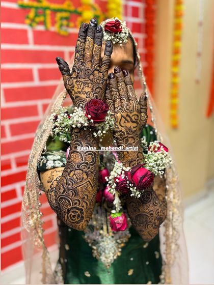 A full bridal look, with the bride's face partially hidden, drawing all attention to the intricate mehendi and floral bracelets.
