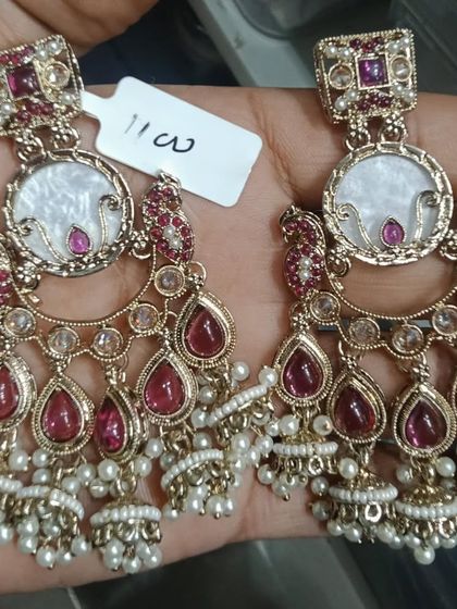 A pair of chandbali earrings with a mother-of-pearl center, ruby-colored stones, and jhumki drops.