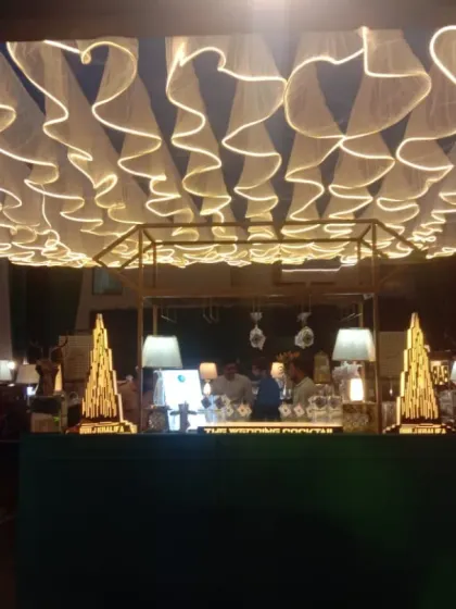 A full view of a bar with a stunning ruffled fabric ceiling installation and multiple neon signs, creating a warm and inviting ambiance for guests.