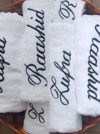 This basket is filled with a complete set of personalized towels for the bride and groom. It includes custom embroidered bath towels, hand towels, and face towels for a coordinated wedding gift.